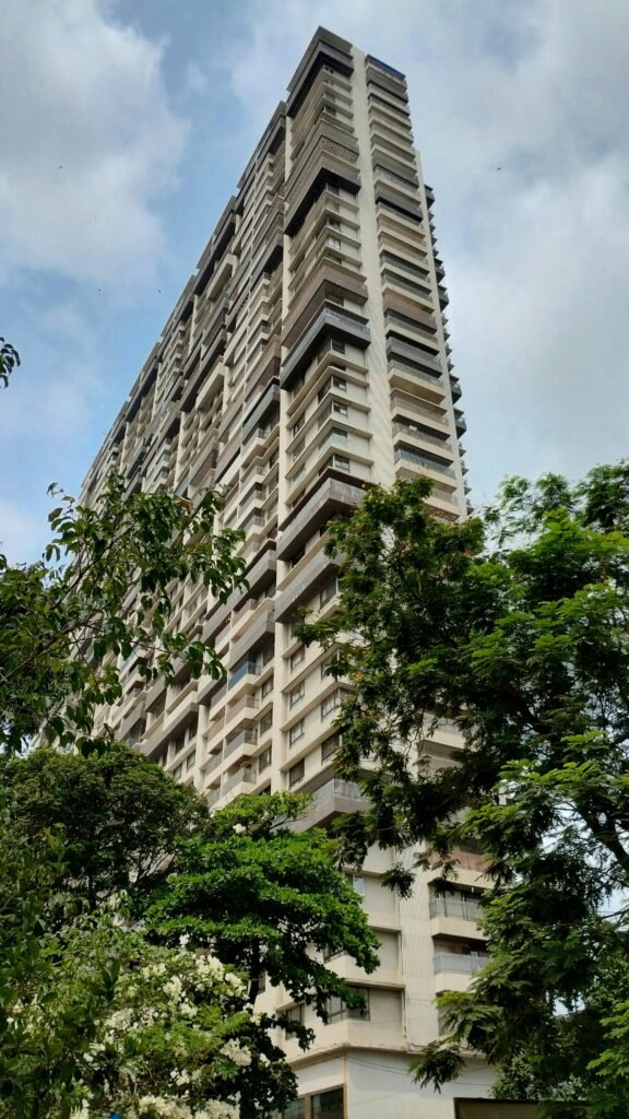 Low angle view of a tall residential building surrounded by trees in Malad, India.