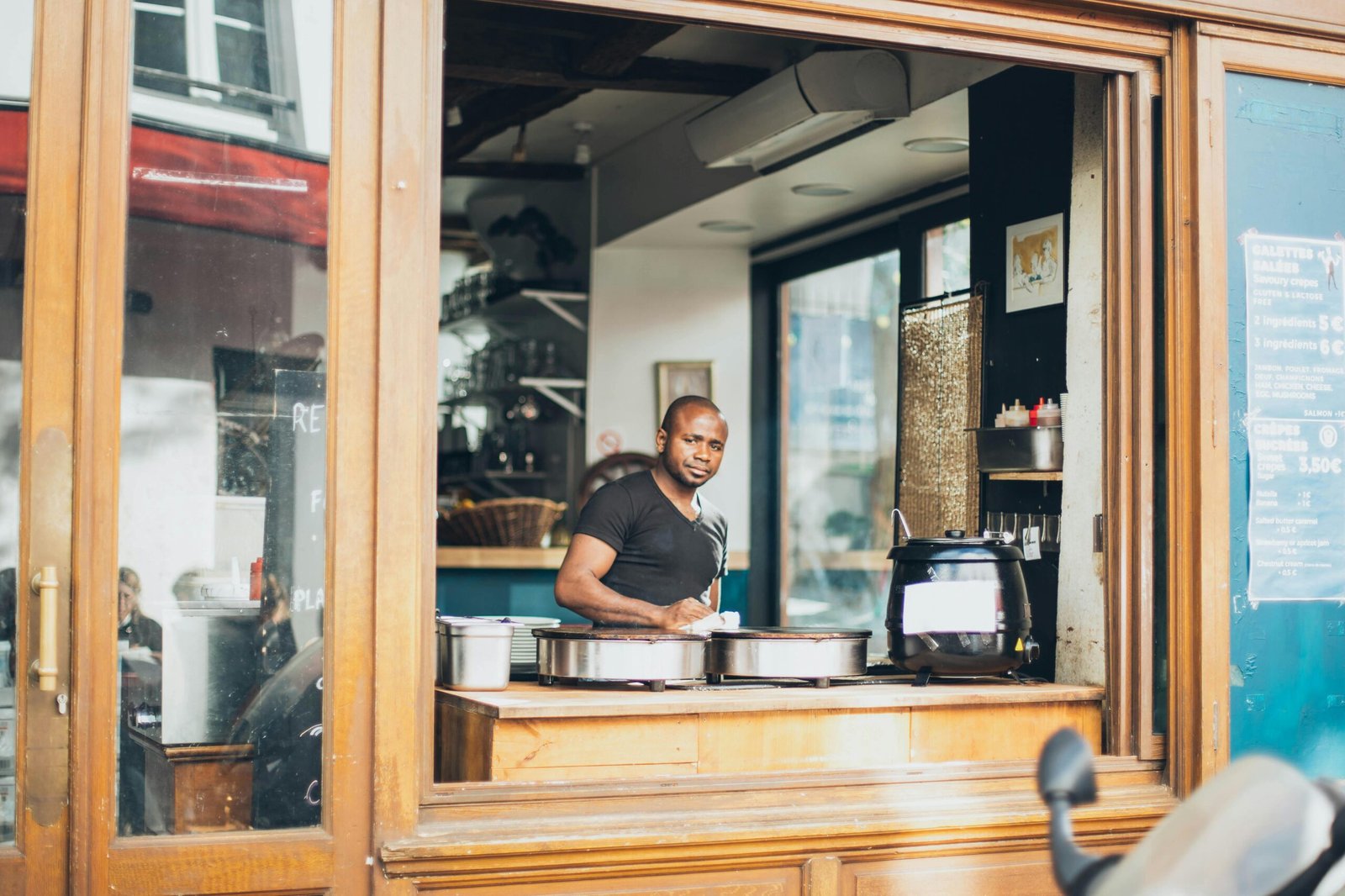 A man stands at the window of a cozy cafe, surrounded by warm wooden interiors.