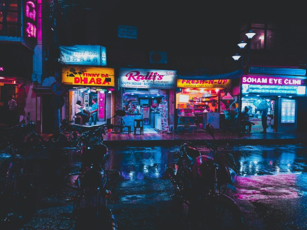 Colorful street scene in Kolkata with glowing shop signs and wet pavement at night.