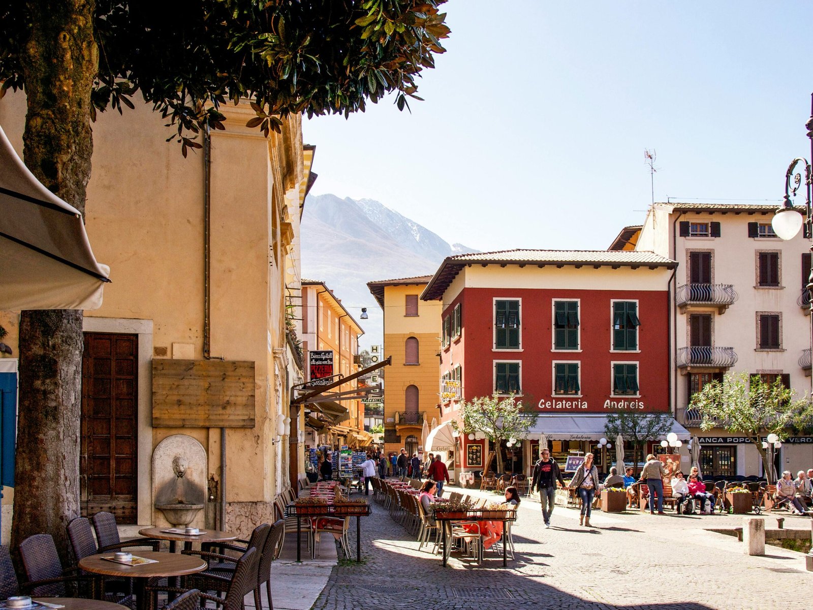 Picturesque Italian street with people enjoying sunny outdoor cafes and shops.