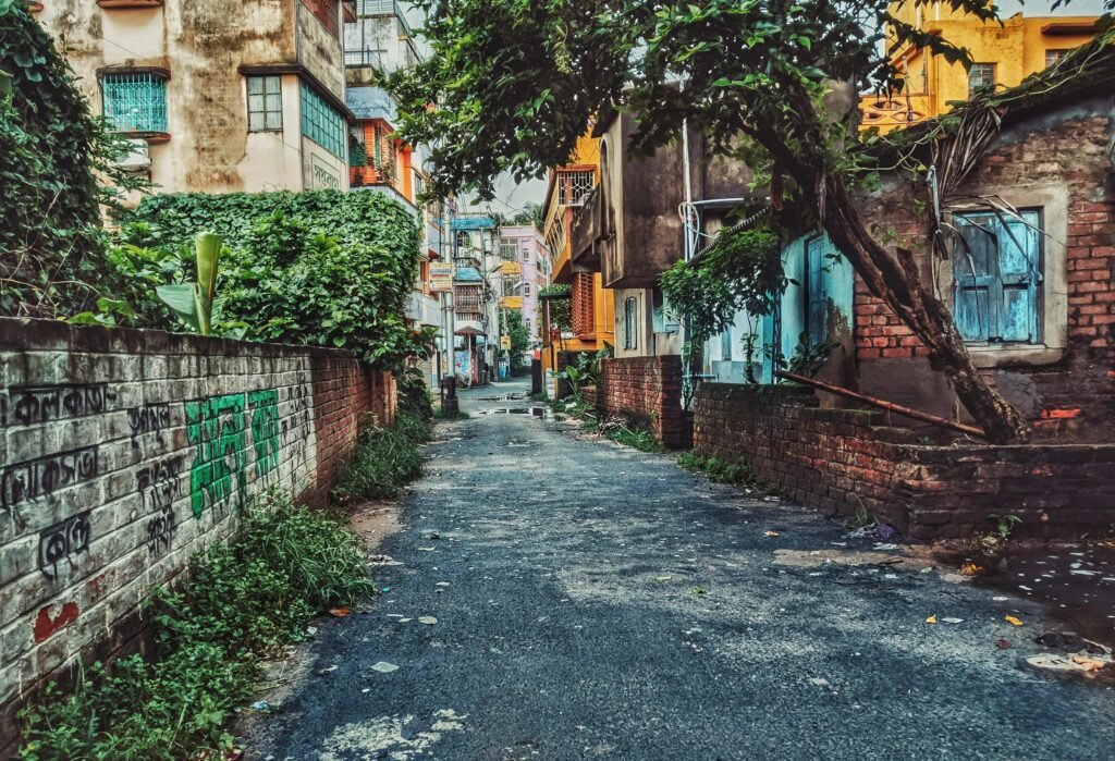 Colorful alleyway in Kolkata, India surrounded by rustic homes and lush greenery, showcasing urban charm.