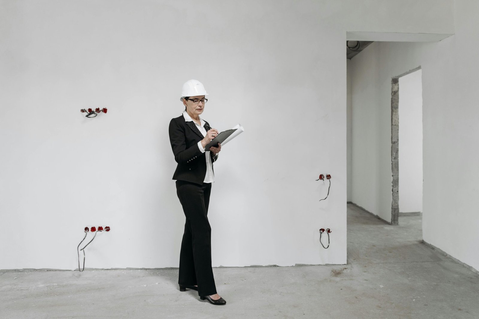 Woman in hard hat reviews notes at a construction site, examining progress.