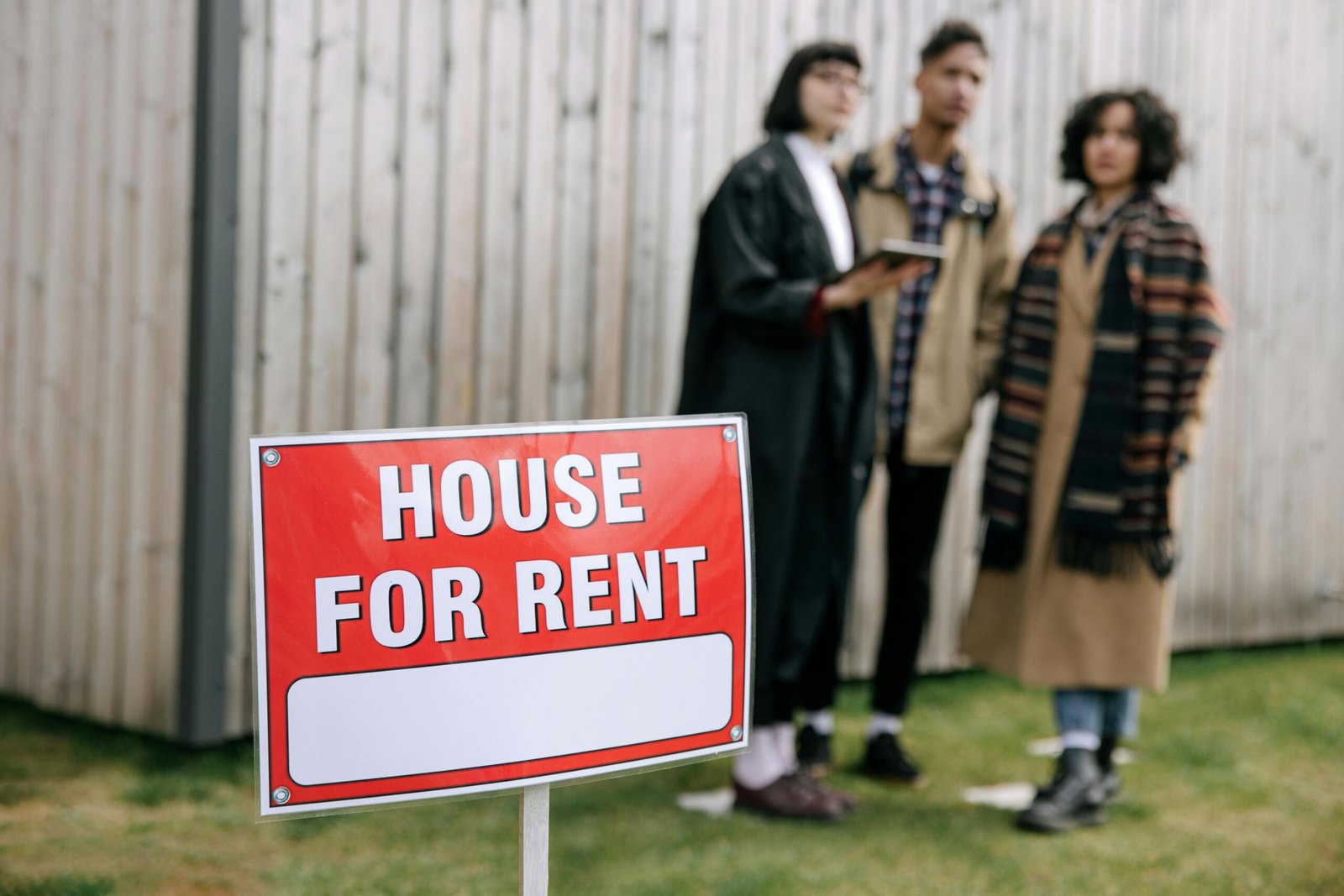 Three adults examining a house for rent sign outdoors, depicting diverse and inclusive interest in rental properties.